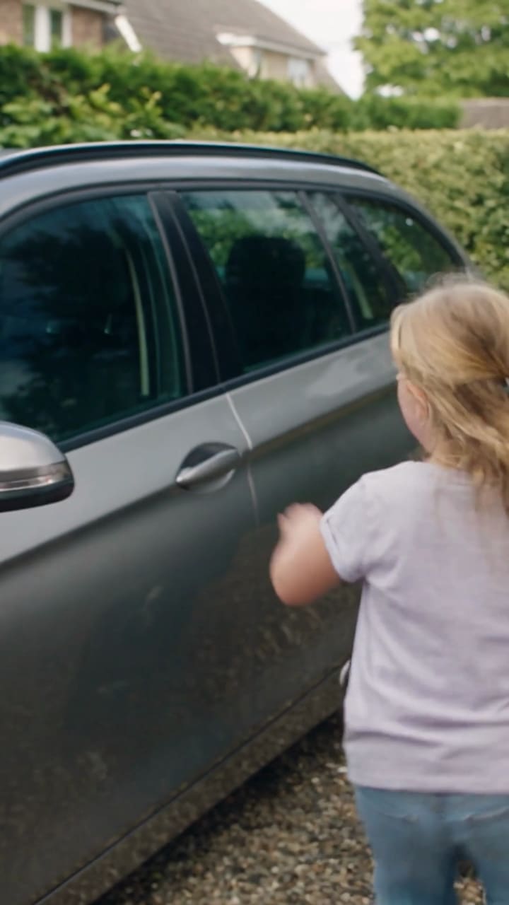 Ein Kind wäscht das Auto in der Einfahrt.